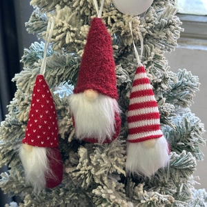 Three Christmas gnome hanging ornaments with red and white knit hats on a snowy pine tree