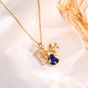 Detailed shot of golden necklace with airplane, blue globe and scroll charms on silk