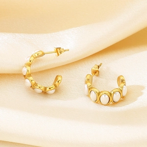 Macro view of C-shaped gold earrings with white pearls on luxury champagne silk