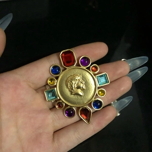 Vintage gold brooch with colorful gems and portrait relief, held for elegant display