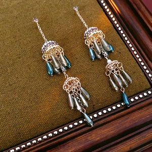 Detail of vintage gold flower earrings with teal beads and tassels on green fabric
