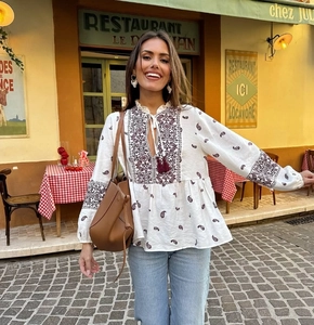 Detail der Bohème-Bluse mit V-Ausschnitt, Ethno-Stickerei und roten Quasten auf weißem Stoff