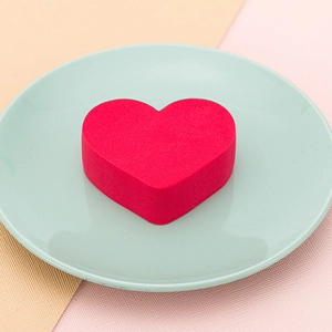 Soft heart-shaped makeup sponge for dry and wet use on a decorative green plate