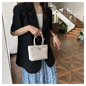 Détail d'un sac seau en nylon crème porté par un mannequin en jupe fleurie et blazer