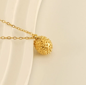 Detailed close-up of 18k gold plated durian pendant necklace on a cream textured surface
