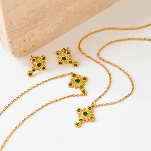 French vintage gold cross jewelry set with green crystals on stone background