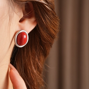 Close-up of red agate earring with silver frame worn by a model in soft lighting