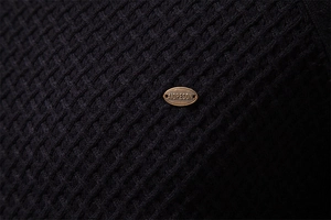 Detail of black waffle knit fabric texture with AIOPESON branded bronze metal tag
