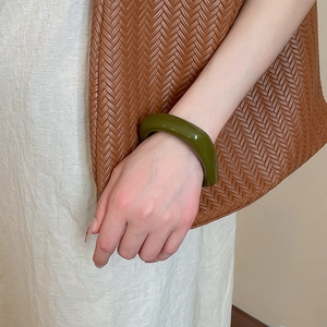 Close-up of a minimalist olive green chunky acrylic bangle worn with a woven bag