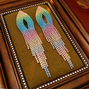 Macro shot of long rainbow gradient rhinestone tassel earrings on green velvet