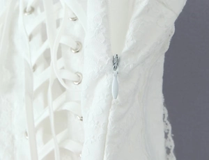 Detailaufnahme des verdeckten Reißverschlusses und der Metallösen an weißem Spitzenkleid