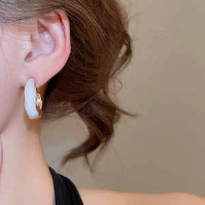 Close-up of a C-shaped earring featuring cream resin and hammered gold metal texture