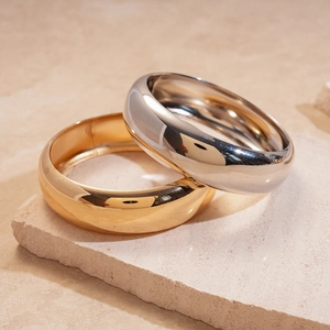 Detail view of stacked gold and silver metallic bangles on a textured stone surface