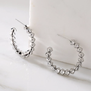 Silver geometric C-shaped earrings with faceted punk rock metallic texture on marble