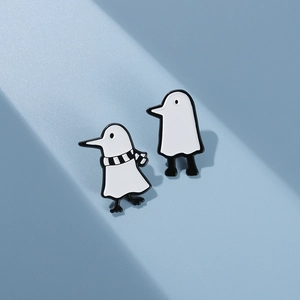 Detailed view of black and white cartoon bird and mushroom enamel pins on a blue surface