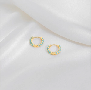 Detail view of gold hoop earrings with sky blue enamel dots on white silk fabric