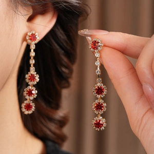 Detail of gold floral tassel earrings with red rhinestones held by a model
