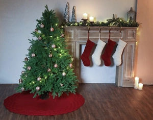 Festive scene with red knitted Christmas tree skirt and matching stockings on a fireplace