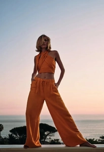 Detail eines orangefarbenen Halterneck-Tops und Leinenhosen auf einem Balkon am Meer