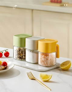 Three square glass spice jars with colorful lids on a marble tray in a kitchen setting