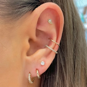 Close-up of stacked gold and silver rhinestone earrings and ear cuffs on model's ear