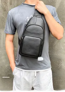 Close-up of black lychee grain leather men's chest bag worn by a model against a wall