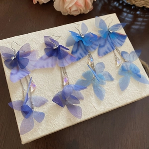 Macro detail of fabric butterfly earrings with long metal tassels and crystal beads