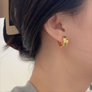 Detail of gold chunky hoop earring with geometric textured surface on model