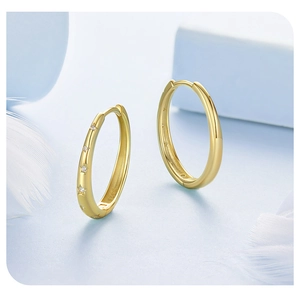 Macro shot of gold oval hoop earrings with star pattern and polished finish