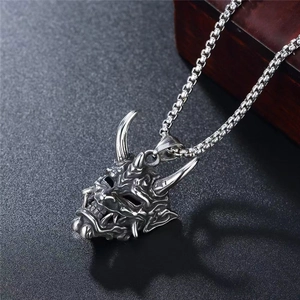 Macro shot of silver metal Prajna mask pendant with intricate texture on dark surface