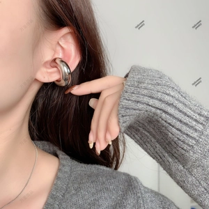 Close-up of a chunky silver hollow ear cuff shown worn with a grey knitted sweater