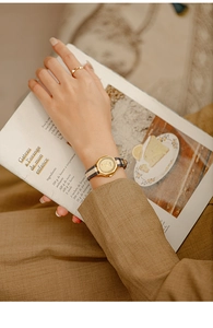 Detail of vintage oval gold watch with beige plaid strap worn by a female model