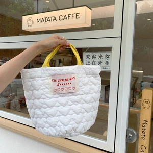 Sac fourre-tout blanc matelassé avec motifs de cœurs et poignées jaunes tenu à la main
