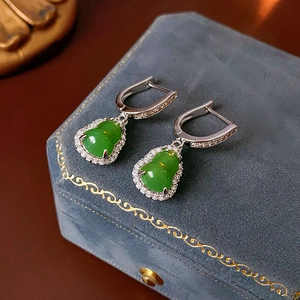Detail of green zircon gourd earring on a blue velvet jewelry box with soft lighting