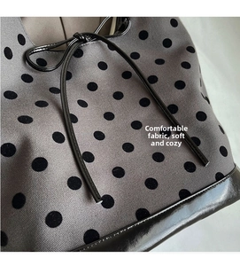 Close-up of grey knit bucket bag fabric with black polka dots and shiny leather drawstring