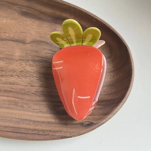 Detail view of a cute orange carrot acrylic hair claw clip on a wooden tray