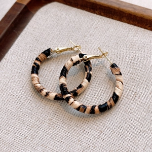 Detailed view of leopard print hoop earrings with textured fabric on a wooden tray