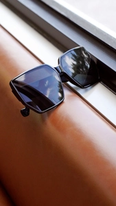 Detail of black oversized square sunglasses on premium brown leather with natural lighting