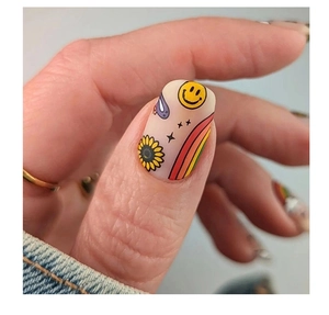 Close-up of matte pop art nail art featuring smiley face, sunflower and rainbow designs