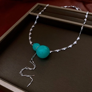 Close-up of heart-link necklace featuring a turquoise gourd pendant and lightning charm
