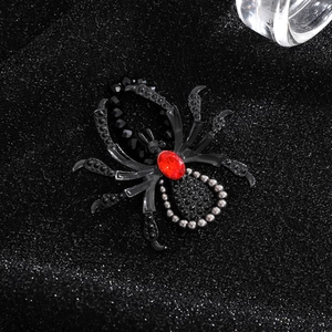 Macro detail of gothic spider brooch featuring a large red gemstone on a dark metal body