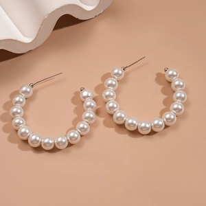 Close-up of elegant C-shaped faux pearl earrings with smooth glossy finish and silver pins