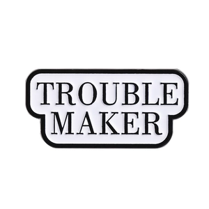 Minimalist enamel Trouble Maker brooch with black text on white background and metal finish