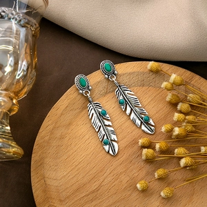 Retro silver feather earrings with turquoise stones on a minimalist wooden tray