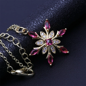 Macro detail of snowflake pendant with red marquise gemstones and 18K gold plated chain
