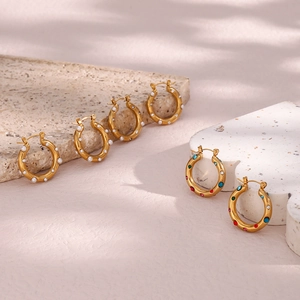 Detailed shot of gold hoop earrings with pearls and multi-color zircon on stone props