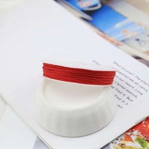 Close-up of bright red hand-woven jewelry cord roll on a white ceramic display