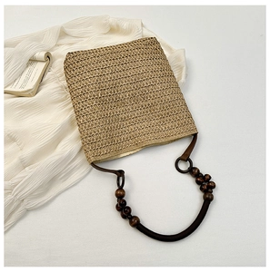Detail of a khaki straw bag with deep brown wooden bead handles on white fabric