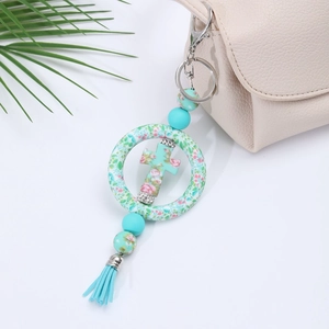 Detail of turquoise silicone cross keychain with floral ring and tassel on a beige bag