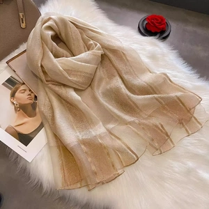 Detail of beige silk wool scarf with metallic gold stripes on white faux fur background